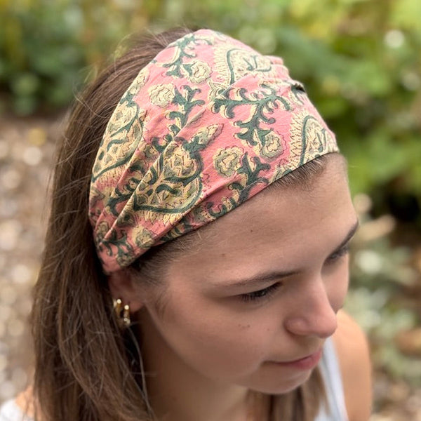 Woman wearing a patterned headband outdoors with greenery in the background