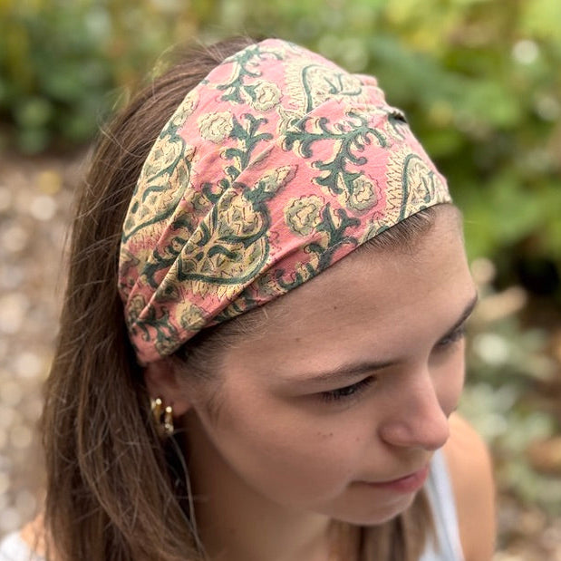 Woman wearing a patterned headband outdoors with greenery in the background