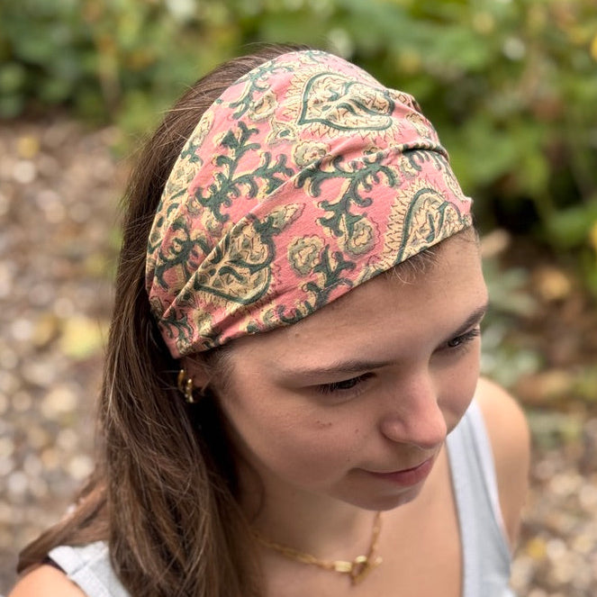 Person wearing a patterned headband outdoors with greenery in the background