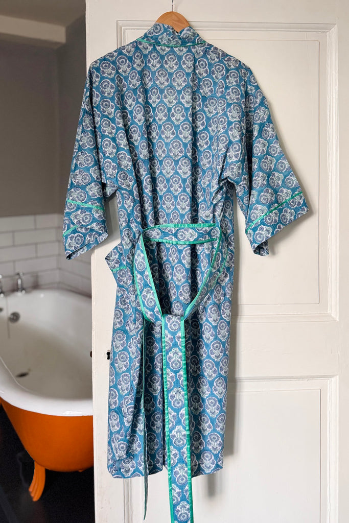 Blue patterned robe hanging on a door next to a bathtub.