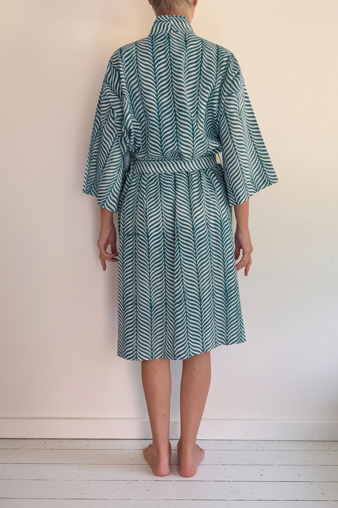 A woman standing with their back to the camera wearing a teal and white patterned kimono robe.