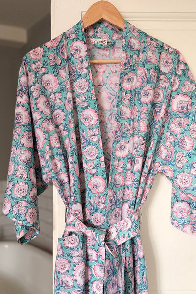 Floral patterned robe hanging on a hanger against a bathroom wall.