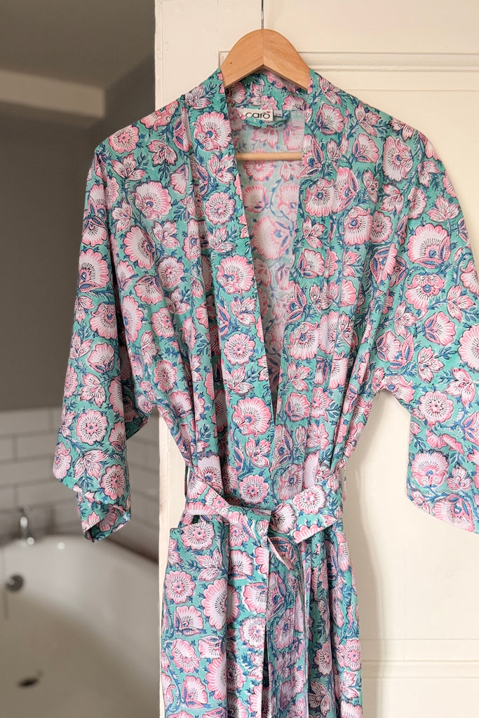 Floral patterned robe hanging on a hanger against a bathroom wall.
