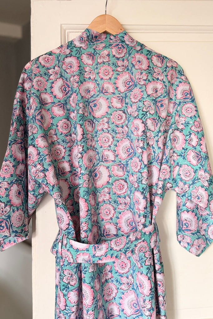 Floral patterned robe hanging on a wooden hanger against a white wall.