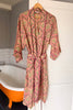 Pink patterned robe hanging on a hook in a bathroom with an orange bathtub.