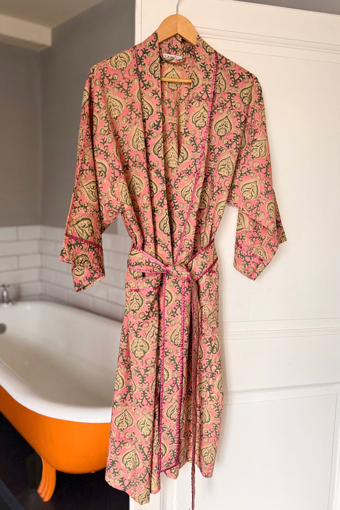 Pink patterned robe hanging on a hook in a bathroom with an orange bathtub.