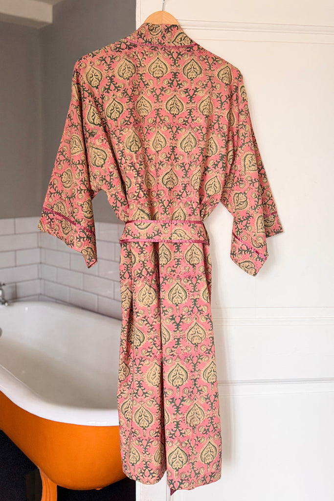 Pink patterned robe hanging on a hook next to a bathtub.