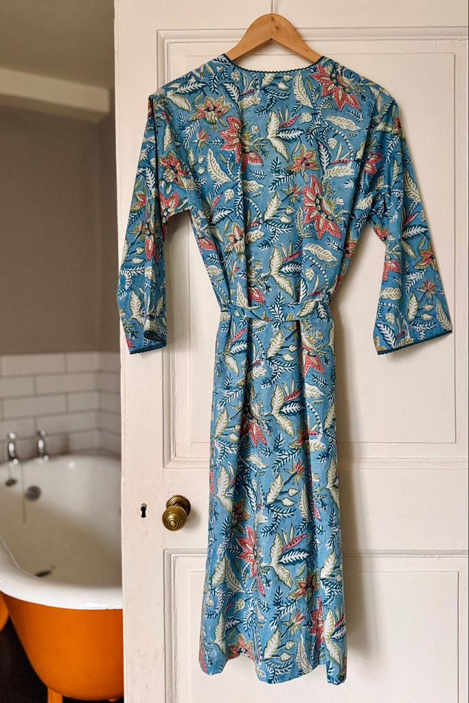 Blue floral patterned robe hanging on a door next to a bathtub.