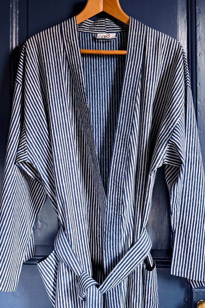 Striped robe hanging on a wooden hanger against a blue wall.