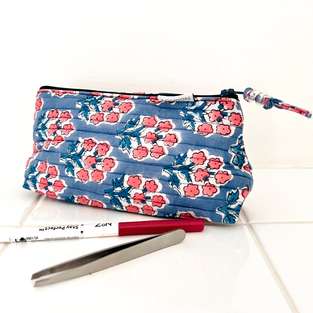 mini make up bag in quilted cotton with small coral pink blossom print on blue ground. Fits into small handbag.  Has white waterproof lining and beaded zip pull. By Caro London.