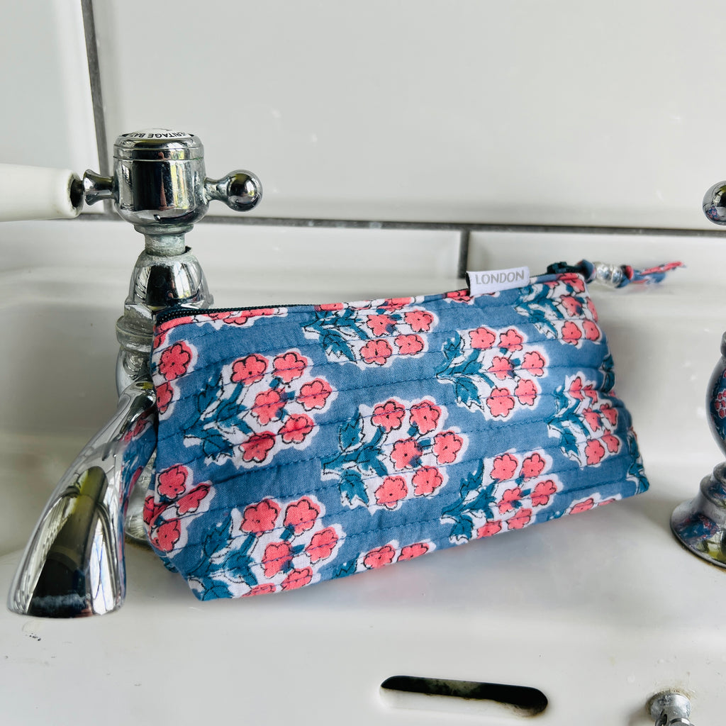 mini make up bag in quilted cotton with small coral pink blossom print on blue ground. Fits into small handbag.  Has white waterproof lining and beaded zip pull. By Caro London.