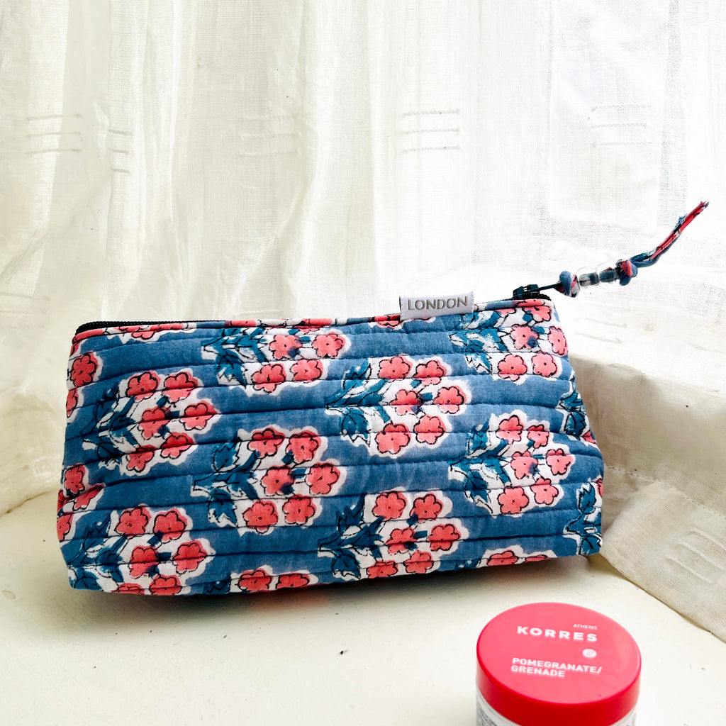 mini make up bag in quilted cotton with small coral pink blossom print on blue ground. Fits into small handbag.  Has white waterproof lining and beaded zip pull. By Caro London.