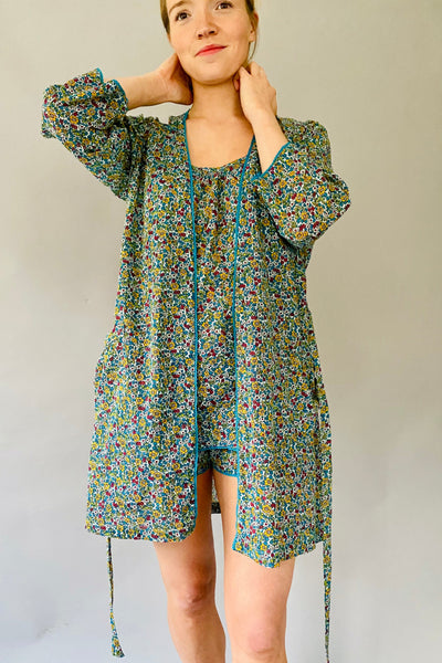Woman wearing Vintage Ditzy floral short kimono robe in blue, yellow and red small floral with blue lace trimmed neckline. Worn over matching camisole and shorts.