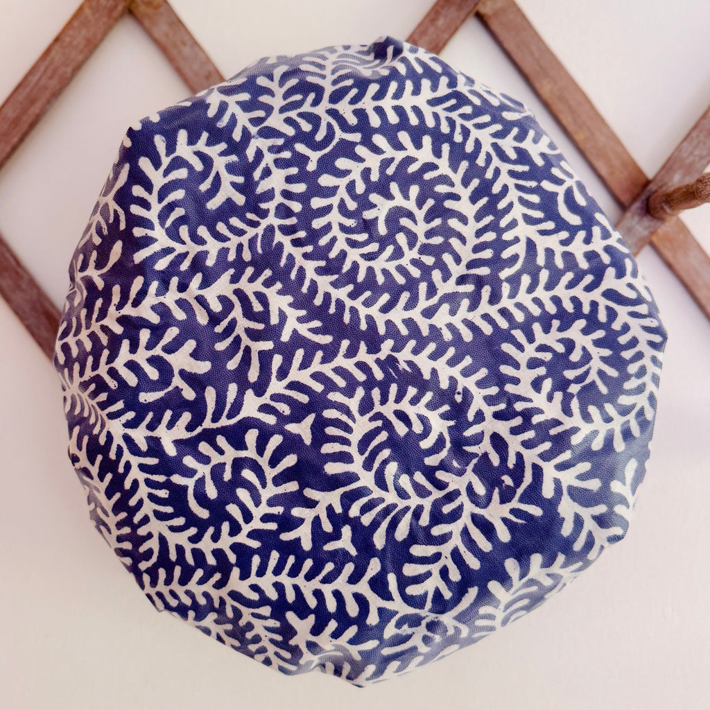 Waterproofed shower cap with a blue and white coral leaf pattern photographed on a wooden lattice wall 