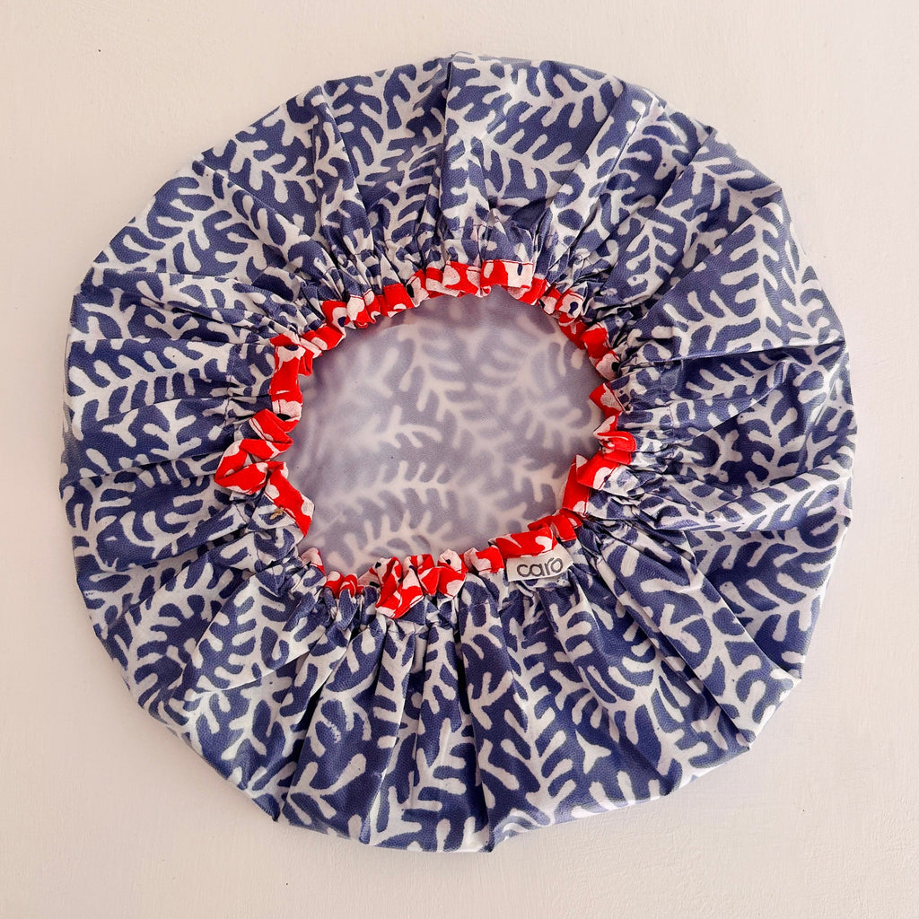 A round shower cap with a  deep blue and white coral branch pattern, featuring a red elasticized inner trim and white lining.
