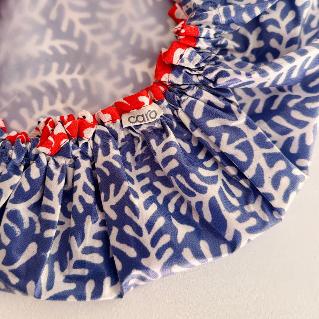 Close-up of a shower cap with a blue and white coral-like pattern, red elasticized trimmed edge and a small visible 'caro' brand tag.