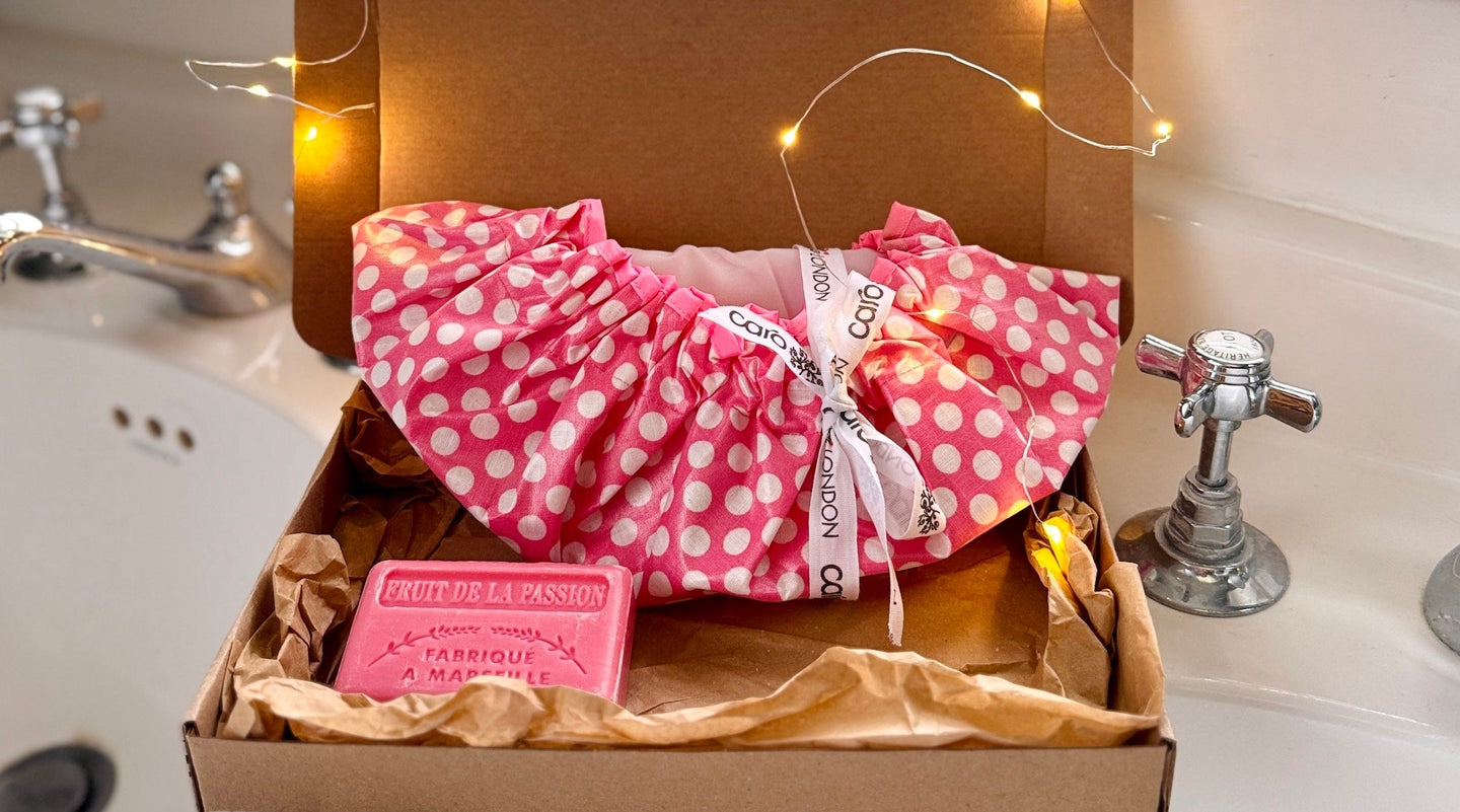 Pink polka dot shower cap and soap in a box with fairy lights on a bathroom counter