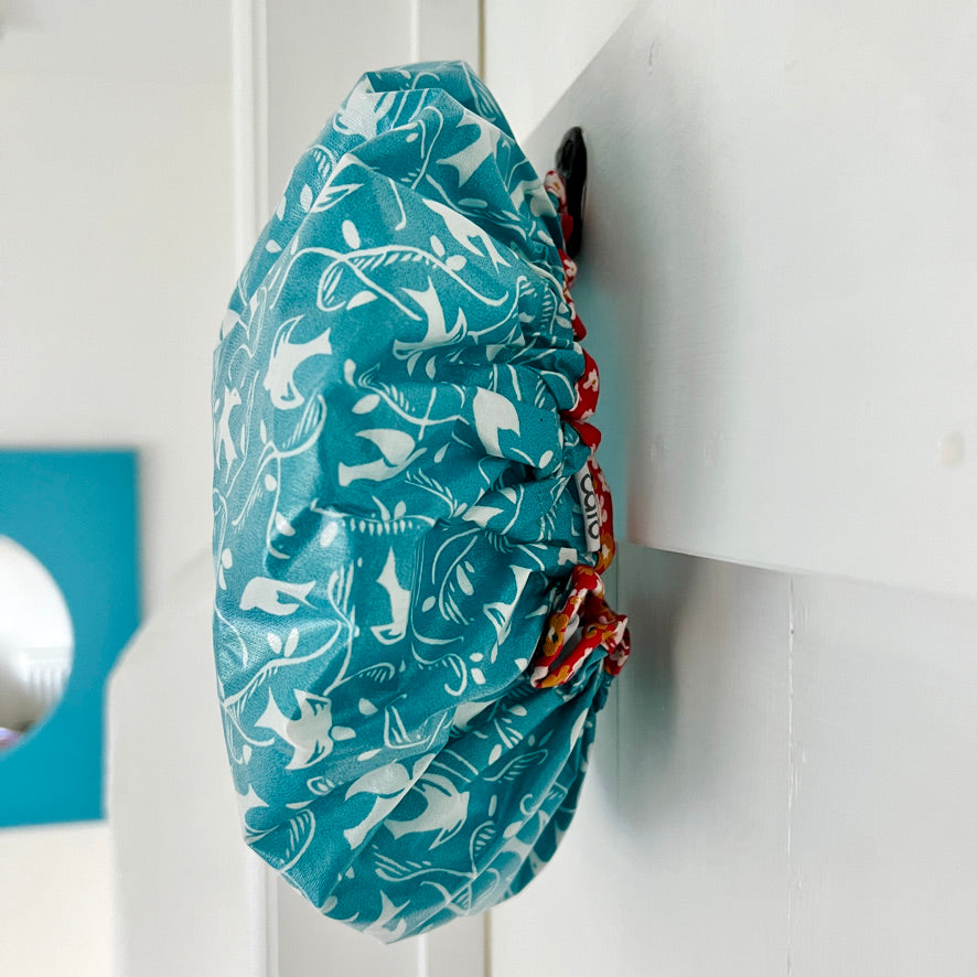close up of best selling teal swallow cotton print waterproofed shower cap hanging up on hook