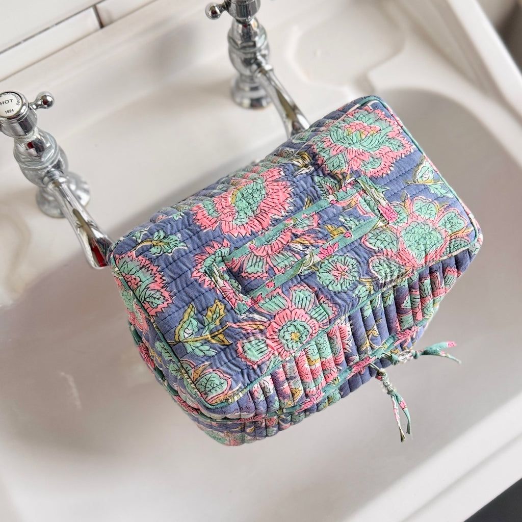 Multicolored  floral quilted boxy toiletry bag sitting on a sink