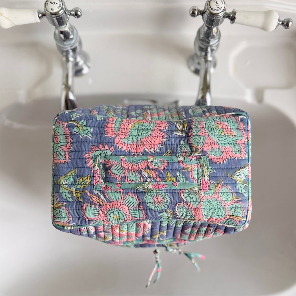 Floral-patterned quilted wash bag sitting on a sink with vintage-style faucet.