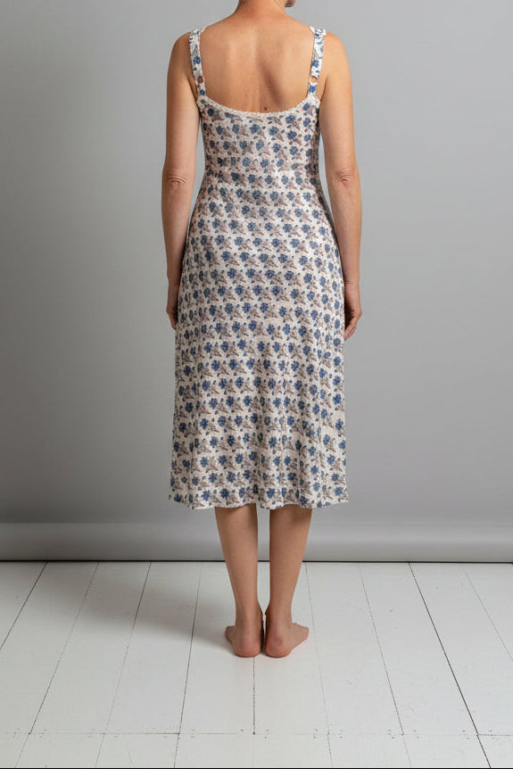 Woman wearing a floral dress standing against a plain wall.