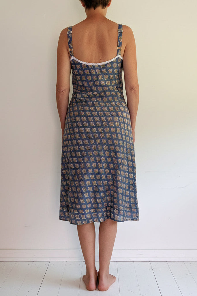Person wearing a blue patterned dress standing against a white wall.