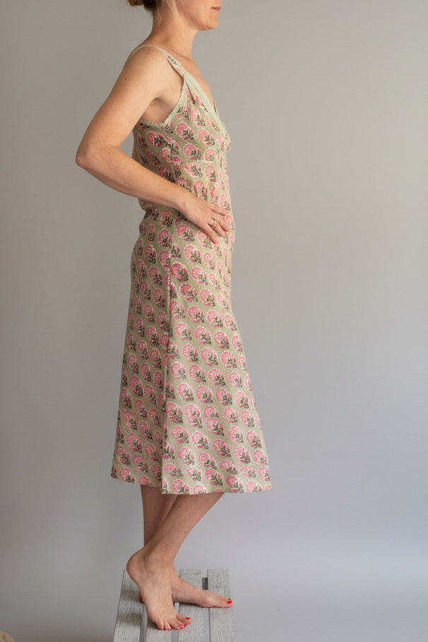 Woman wearing a floral nightgown standing against a white wall.
