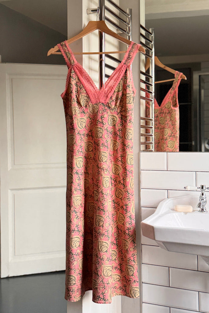 Pink patterned nightdress hanging on a wooden hanger in a bathroom.