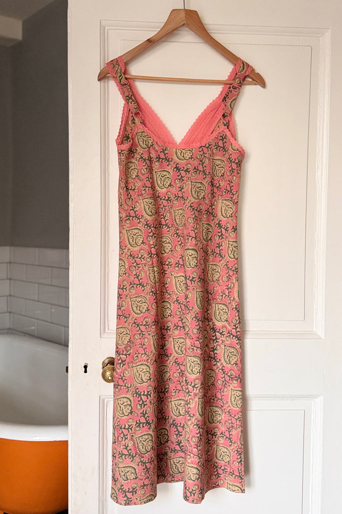 Pink floral nightie hanging on a wooden hanger against a white door.