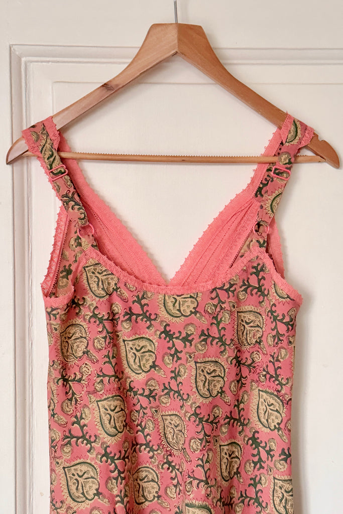Pink dress with black floral pattern on a wooden hanger against a white wall.