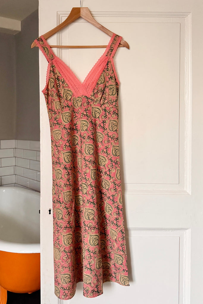 Pink floral nightie hanging on a wooden hanger against a white door.