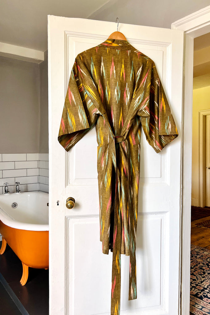 Colorful robe hanging on a white door with a bathtub and tiled wall in the background.