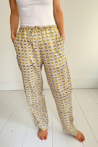 A person wearing wide legged pajama bottoms with a daisy chain pattern in yellow, green, and cream colors.