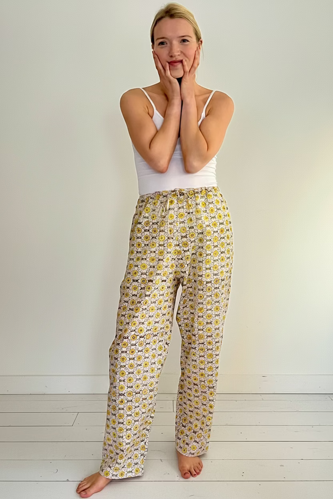 A woman wearing wide legged pajama bottoms with a daisy chain pattern in yellow, green, and cream colors.