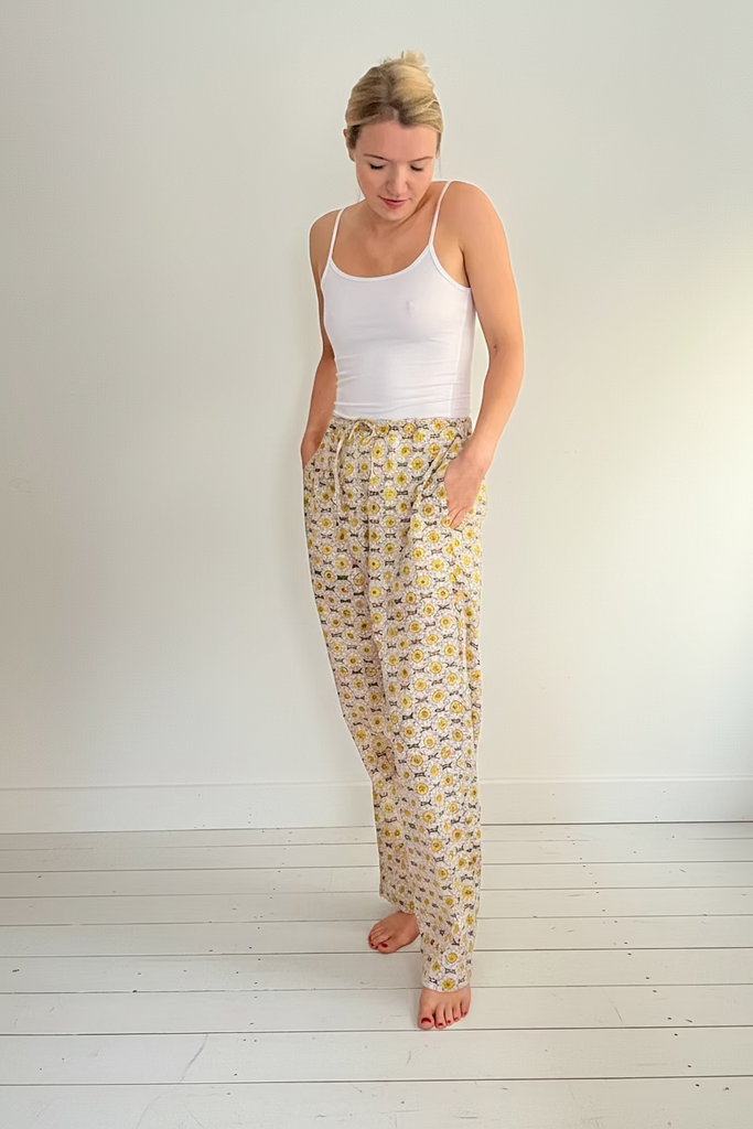 A person wearing wide legged pajama bottoms with a daisy chain pattern in yellow, green, and cream colors.