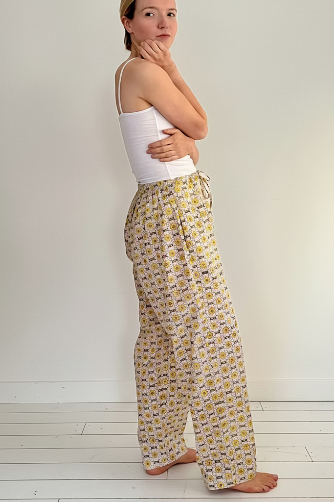 Side view of woman wearing wide legged pajama bottoms with a daisy chain pattern in yellow, green, and cream colors.
