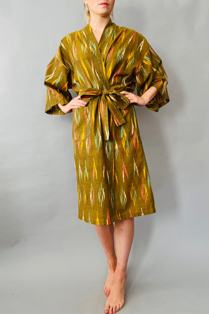 woman wearing a gold and green patterned robe on a grey background
